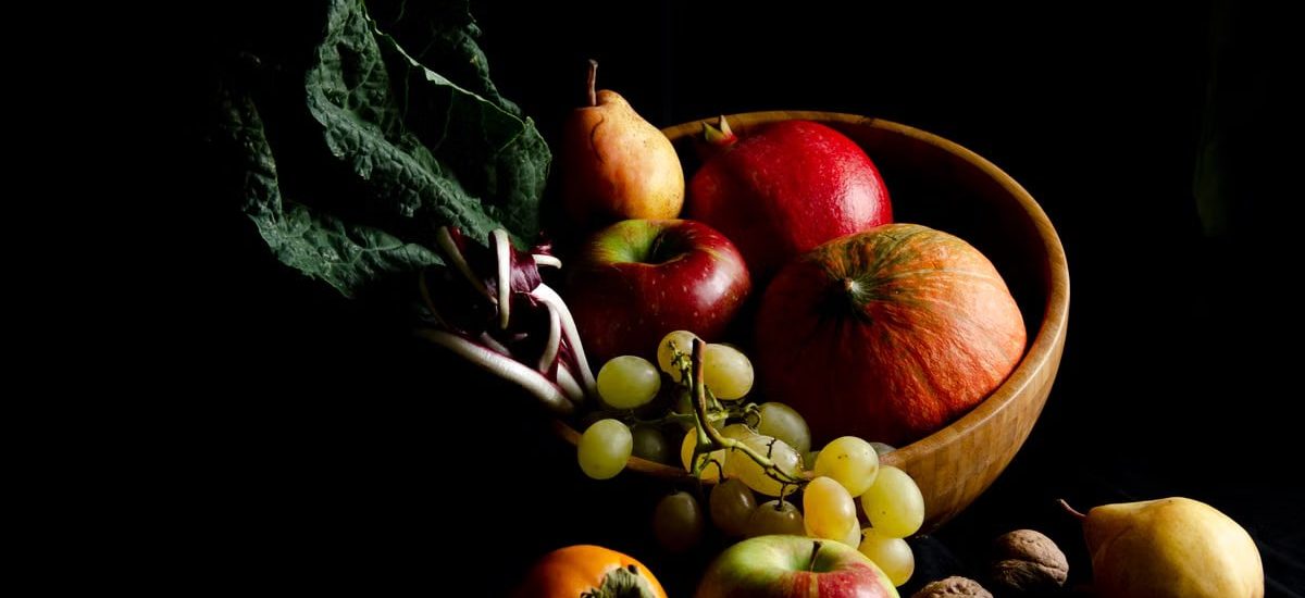 Dark still life composition featuring assorted autumn fruits in a wooden bowl, creating a moody and artistic scene.