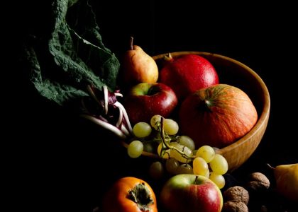 Dark still life composition featuring assorted autumn fruits in a wooden bowl, creating a moody and artistic scene.